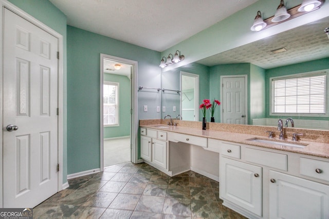 bathroom featuring a sink, a textured ceiling, baseboards, and double vanity