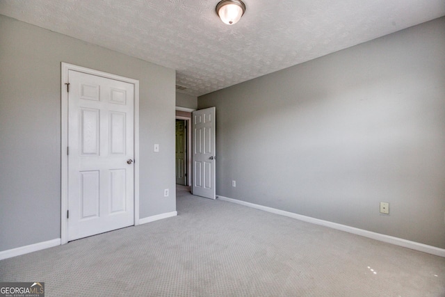 unfurnished bedroom featuring baseboards, a textured ceiling, and light colored carpet