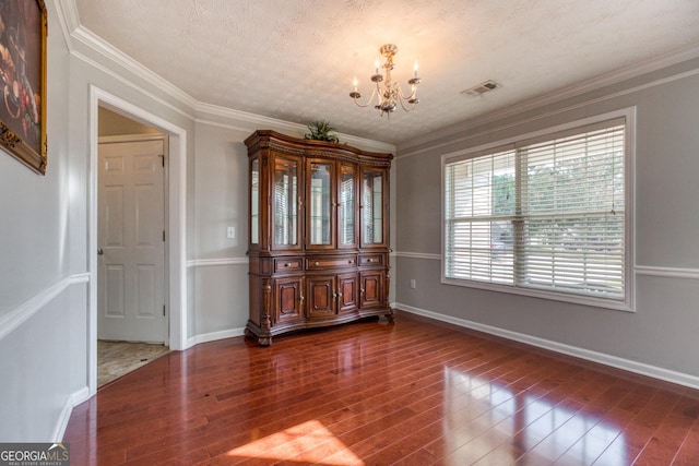 unfurnished dining area featuring a notable chandelier, visible vents, dark wood-type flooring, and ornamental molding