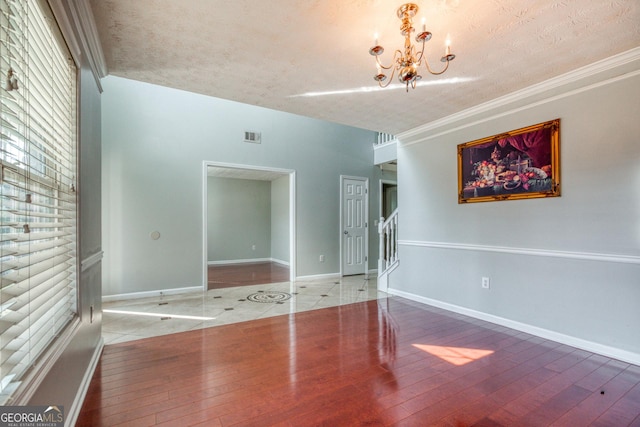 spare room with an inviting chandelier, ornamental molding, wood finished floors, baseboards, and stairs