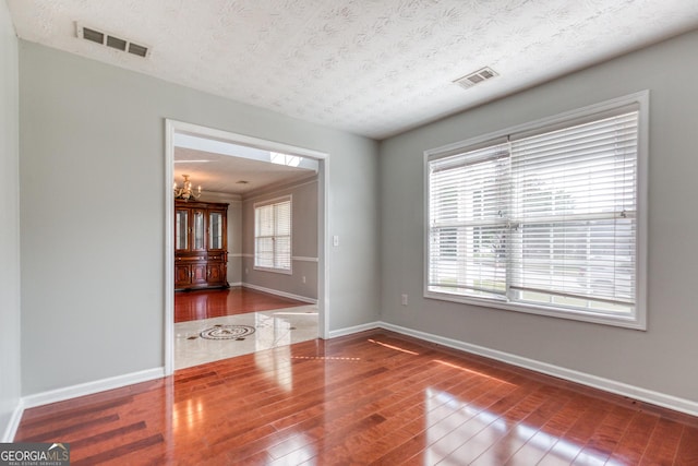 unfurnished room with visible vents, a textured ceiling, baseboards, and wood finished floors