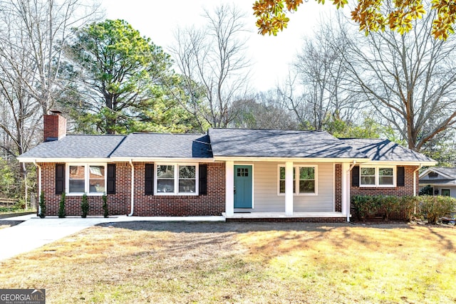 ranch-style home with brick siding, a chimney, a porch, a shingled roof, and a front lawn