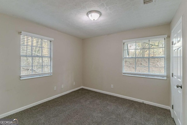 spare room with baseboards, visible vents, dark carpet, and a textured ceiling