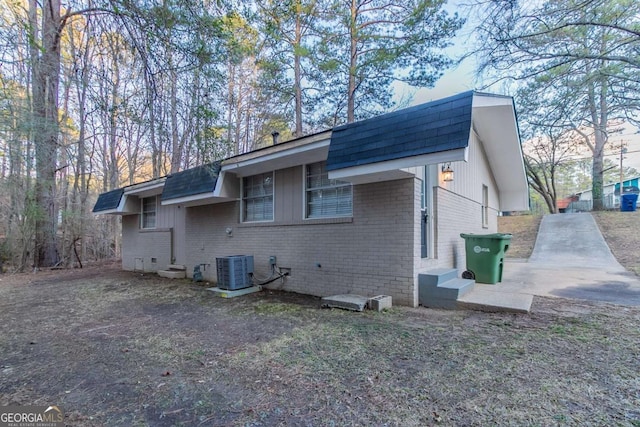 view of home's exterior with a shingled roof, cooling unit, and brick siding