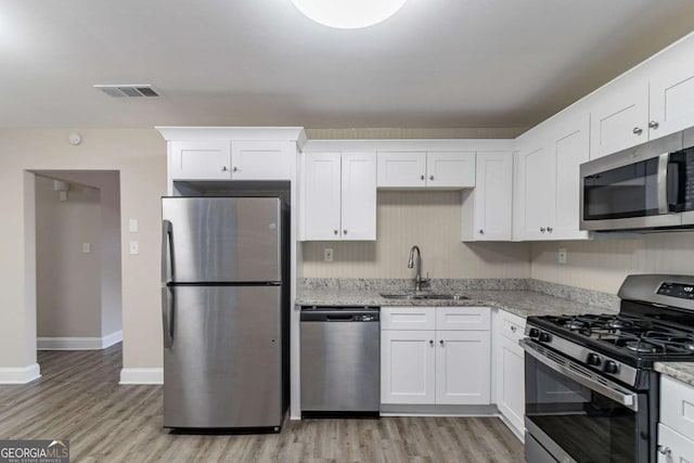 kitchen featuring appliances with stainless steel finishes, a sink, light stone counters, and white cabinets