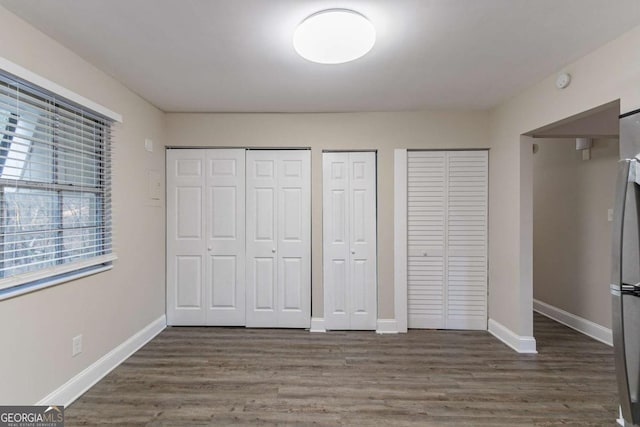 unfurnished bedroom with two closets, dark wood finished floors, and baseboards