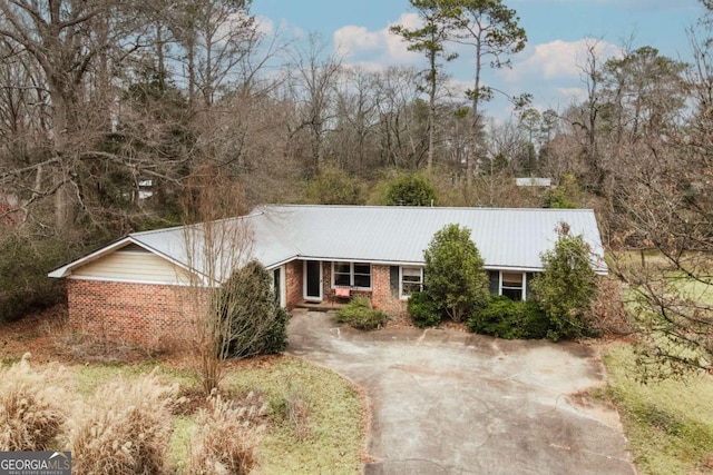 ranch-style house featuring concrete driveway, brick siding, and metal roof