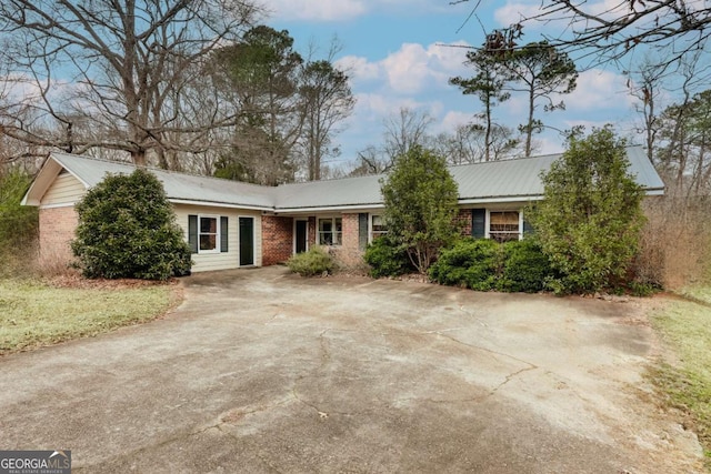 single story home with metal roof, brick siding, and driveway