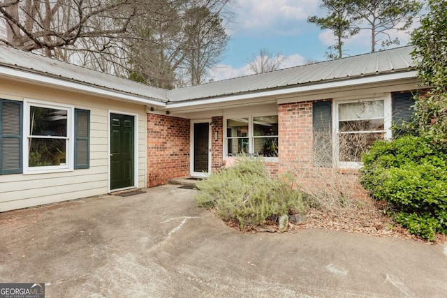 view of exterior entry featuring a patio area, brick siding, and metal roof