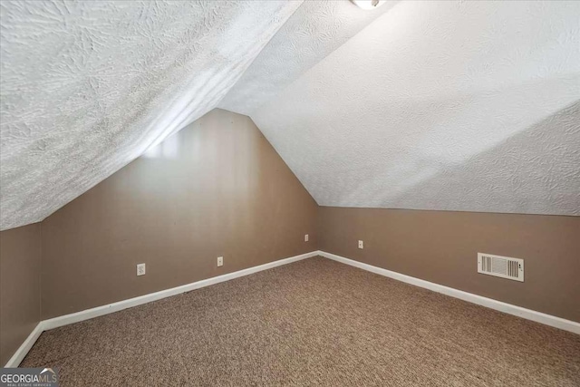 bonus room with a textured ceiling, lofted ceiling, carpet flooring, visible vents, and baseboards