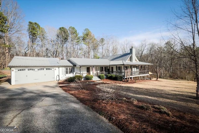 view of front of home featuring metal roof, covered porch, a garage, driveway, and a chimney