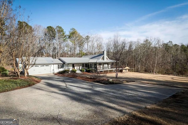 view of front facade with a porch, driveway, a chimney, and an attached garage