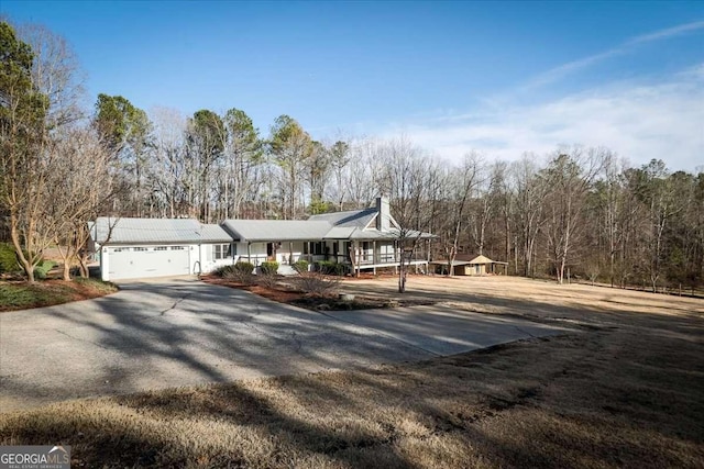 view of front of home with a garage, covered porch, driveway, and a chimney