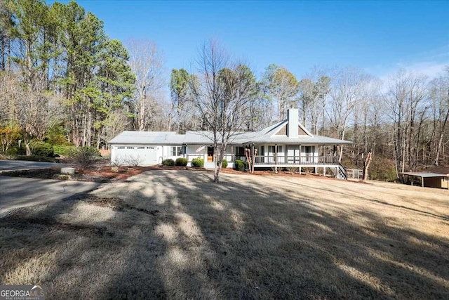 view of front of property with a garage, covered porch, driveway, and a chimney