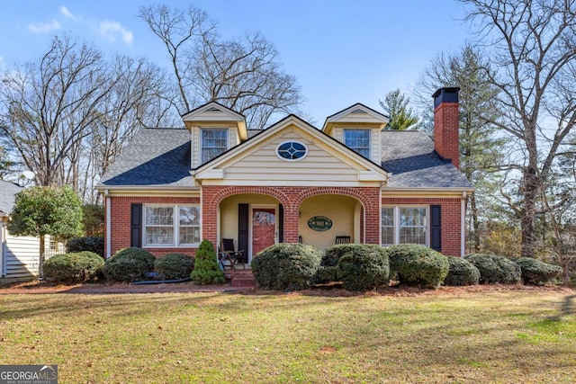 view of front of house with a shingled roof, a chimney, a front lawn, and brick siding