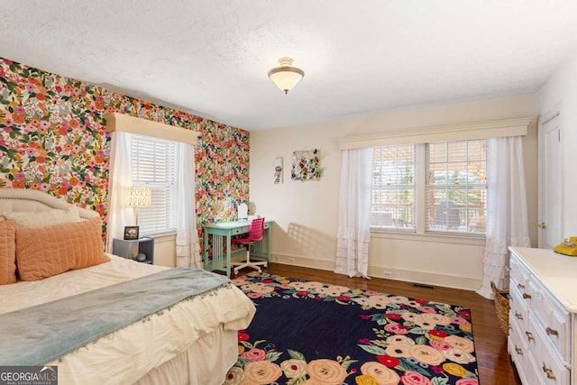 bedroom with wallpapered walls, a textured ceiling, baseboards, and wood finished floors