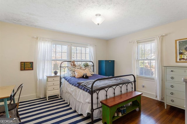 bedroom with multiple windows, baseboards, a textured ceiling, and wood finished floors