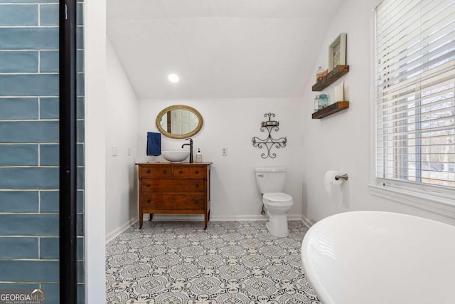 full bathroom with a freestanding tub, toilet, vanity, baseboards, and vaulted ceiling