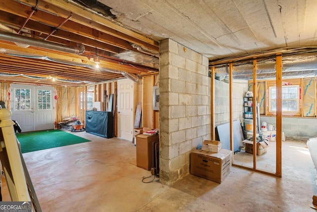 basement with a wealth of natural light, electric panel, and concrete block wall