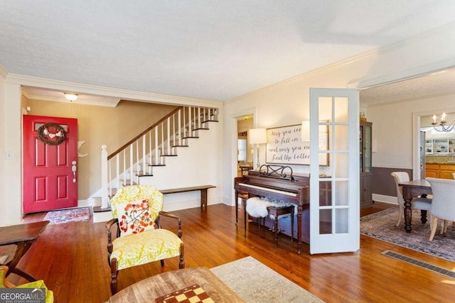 foyer with crown molding, a notable chandelier, visible vents, wood finished floors, and stairs