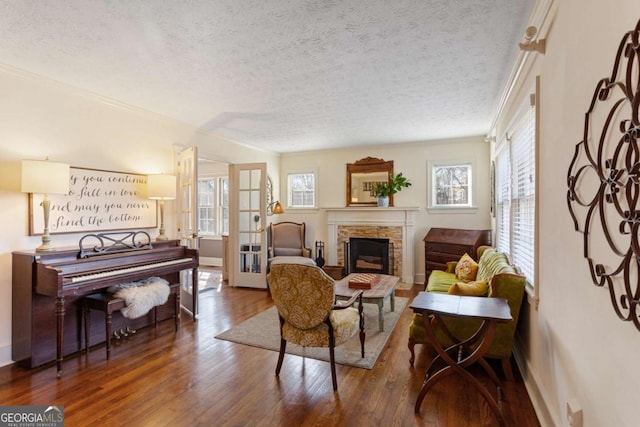 living room featuring a fireplace with raised hearth, a textured ceiling, wood-type flooring, and a wealth of natural light