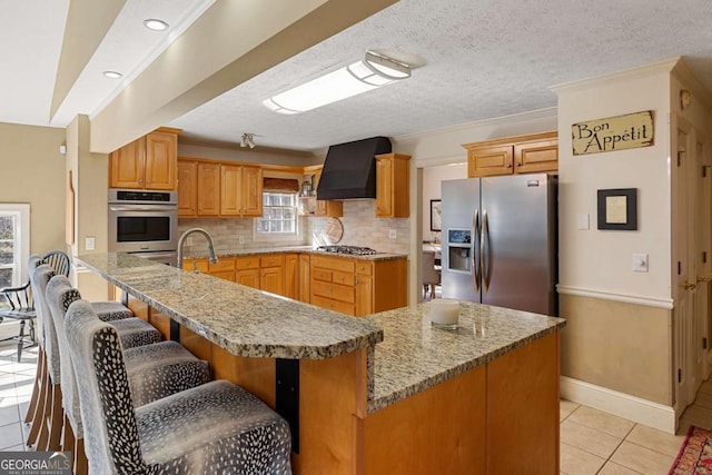 kitchen featuring light tile patterned flooring, exhaust hood, appliances with stainless steel finishes, backsplash, and a kitchen bar