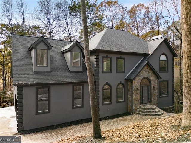 view of front facade featuring a shingled roof, stone siding, and stucco siding