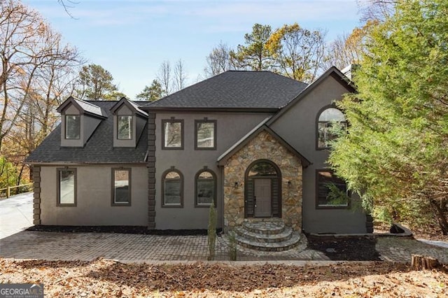 view of front of house featuring a shingled roof, stone siding, a patio area, and stucco siding