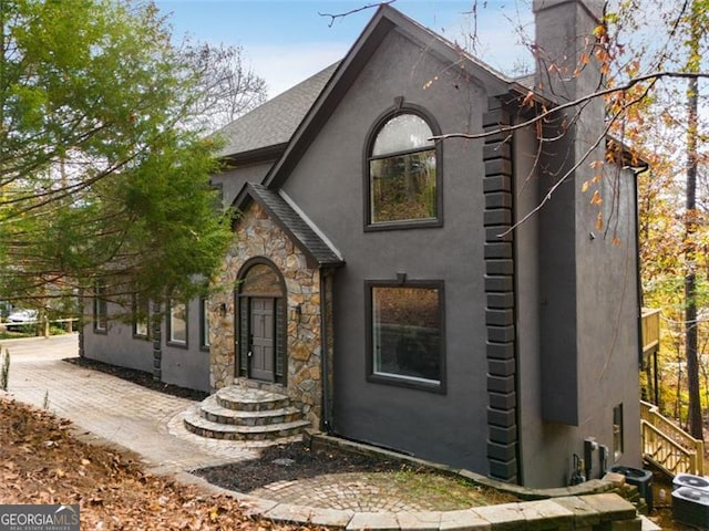 view of front of house featuring stone siding, a chimney, and stucco siding