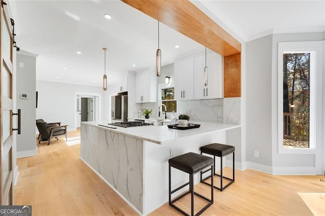 kitchen with a breakfast bar area, a peninsula, white cabinetry, light countertops, and decorative light fixtures