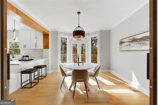 dining area featuring light wood finished floors, visible vents, baseboards, crown molding, and french doors