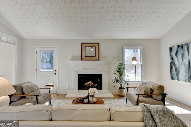 living area featuring a fireplace with raised hearth, a textured ceiling, wood finished floors, and baseboards