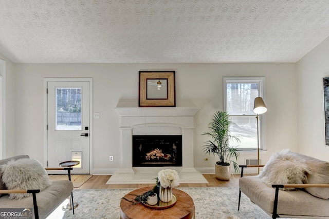 living area with a fireplace with raised hearth, a textured ceiling, wood finished floors, visible vents, and baseboards