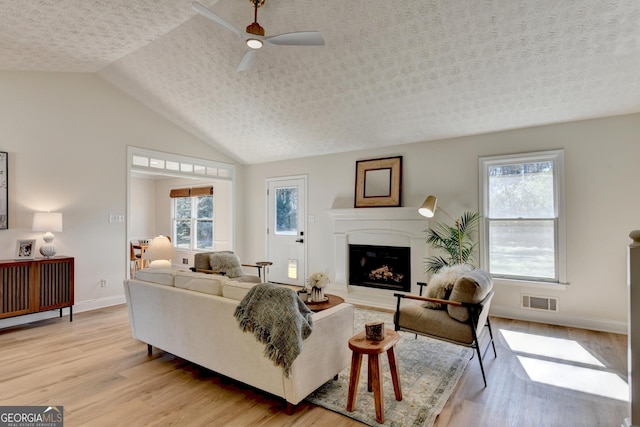 living room with visible vents, lofted ceiling, light wood-style flooring, a textured ceiling, and a fireplace