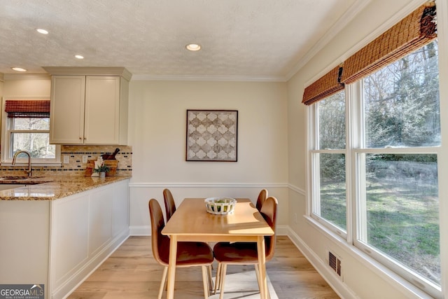 dining area featuring a textured ceiling, light wood finished floors, ornamental molding, and visible vents