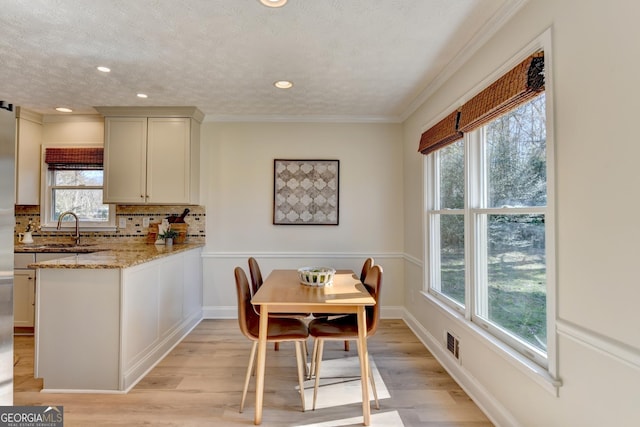 dining space featuring visible vents, crown molding, light wood-style flooring, and a textured ceiling