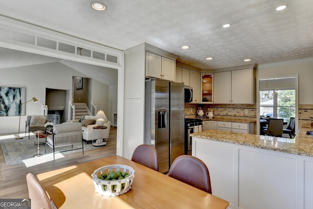 kitchen with tasteful backsplash, light wood-style flooring, a peninsula, light stone countertops, and stainless steel appliances