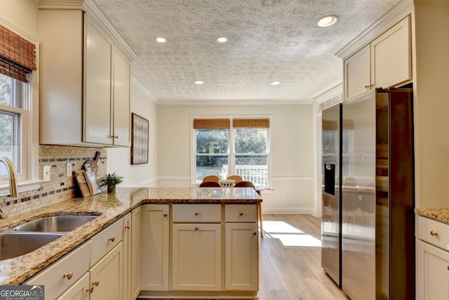 kitchen featuring decorative backsplash, ornamental molding, a peninsula, stainless steel refrigerator with ice dispenser, and a sink