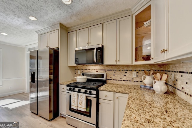 kitchen with appliances with stainless steel finishes, glass insert cabinets, decorative backsplash, and light stone countertops