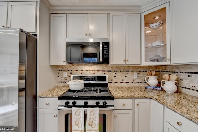 kitchen with appliances with stainless steel finishes, glass insert cabinets, backsplash, and light stone countertops