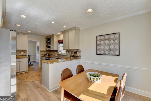 kitchen featuring a peninsula, a sink, freestanding refrigerator, open shelves, and light wood finished floors