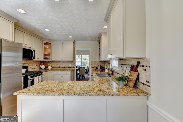 kitchen with light stone counters, decorative backsplash, appliances with stainless steel finishes, a sink, and a peninsula