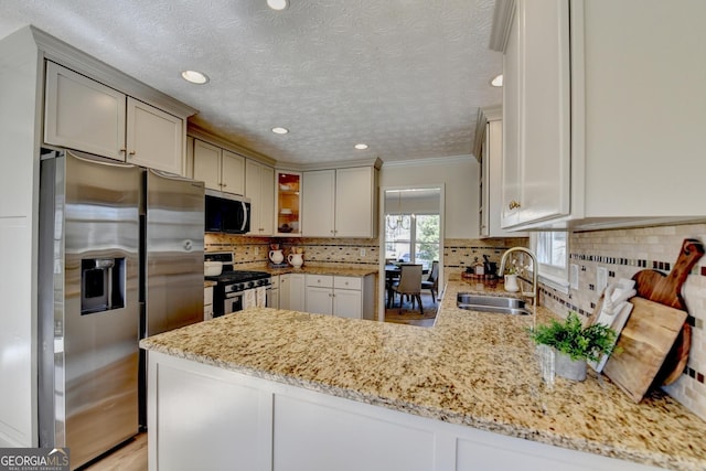 kitchen with a peninsula, a sink, light stone countertops, stainless steel appliances, and backsplash