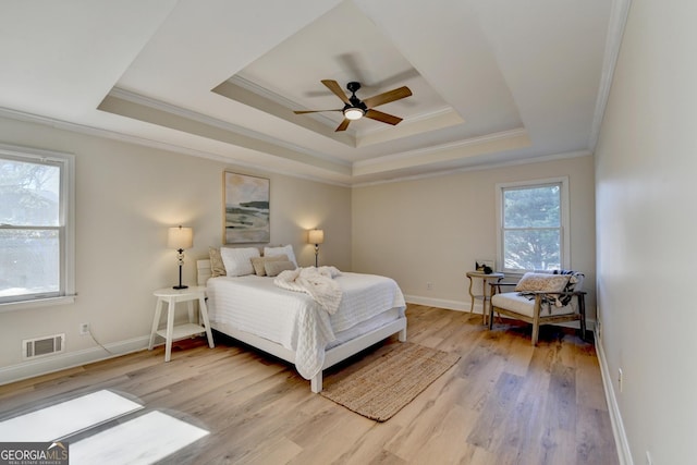 bedroom with light wood-style floors, visible vents, a raised ceiling, and ornamental molding