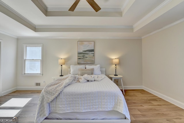 bedroom featuring wood finished floors, ornamental molding, a raised ceiling, and baseboards