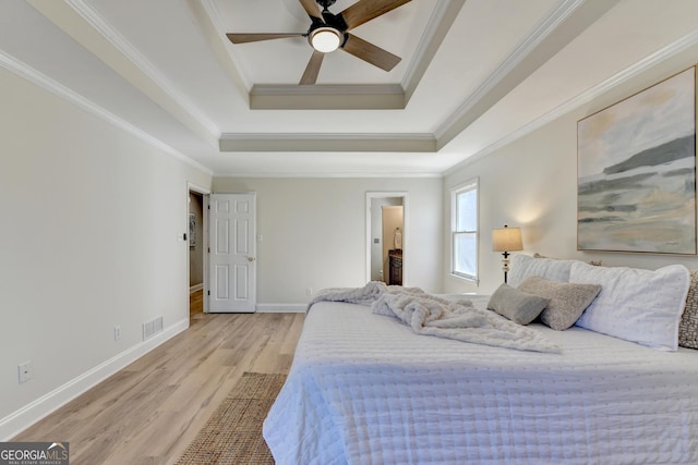 bedroom with baseboards, visible vents, a raised ceiling, crown molding, and light wood-type flooring