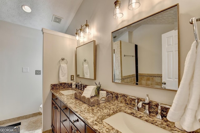 bathroom featuring double vanity, a textured ceiling, visible vents, and a sink