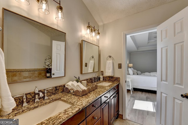 ensuite bathroom featuring double vanity, ensuite bath, a textured ceiling, and a sink