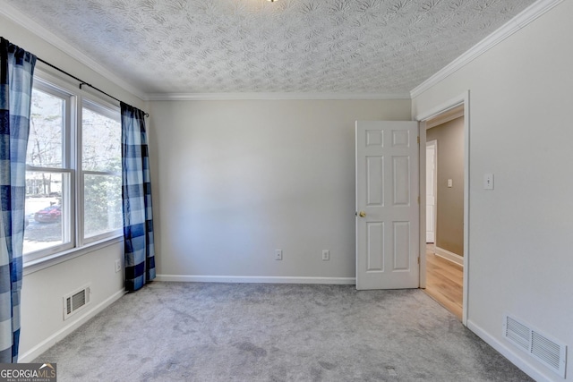 carpeted spare room with a textured ceiling, ornamental molding, visible vents, and baseboards