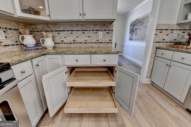 kitchen with light stone counters, backsplash, light wood-style floors, a textured ceiling, and gas range